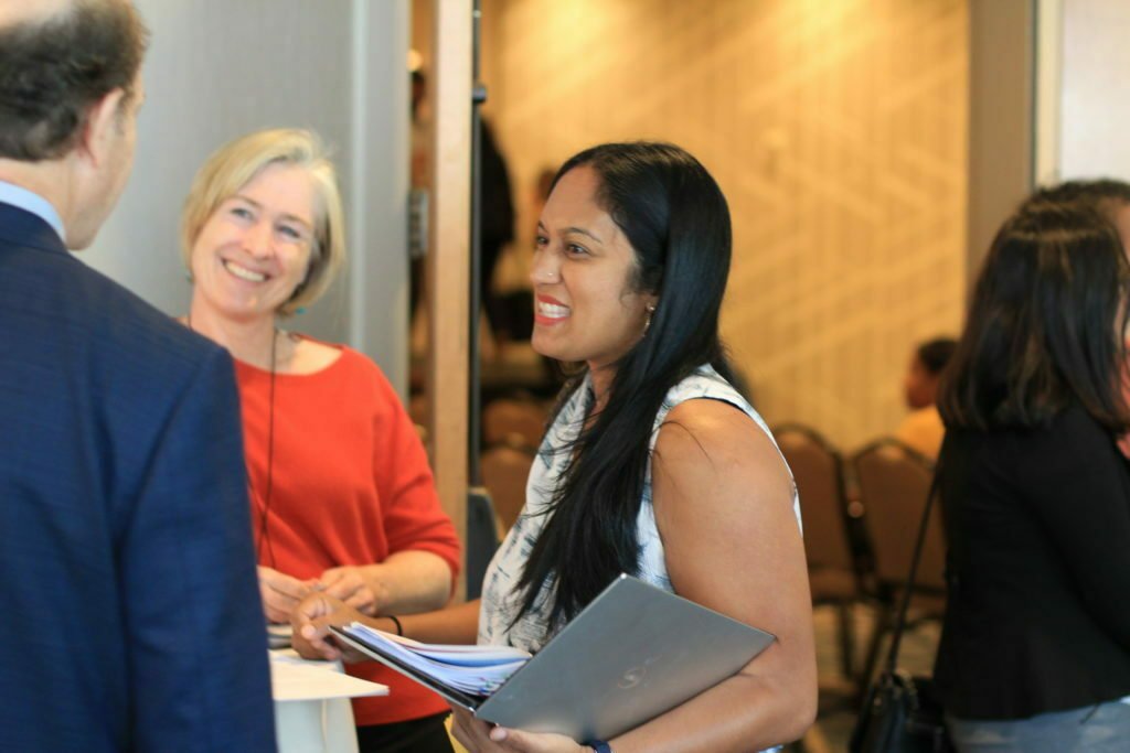 A smiling woman with long black hair is talking to two other people.