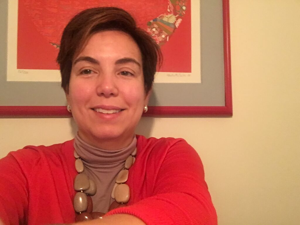 Color photo of a woman in a bright orange-red sweater and a red-framed photo in the background that matches the color of her sweater.