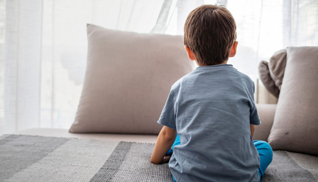 young boy sitting on bed, looking out window