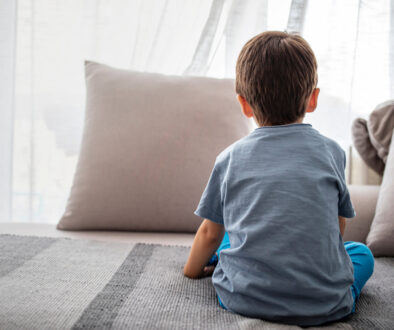 young boy sitting on bed, looking out window