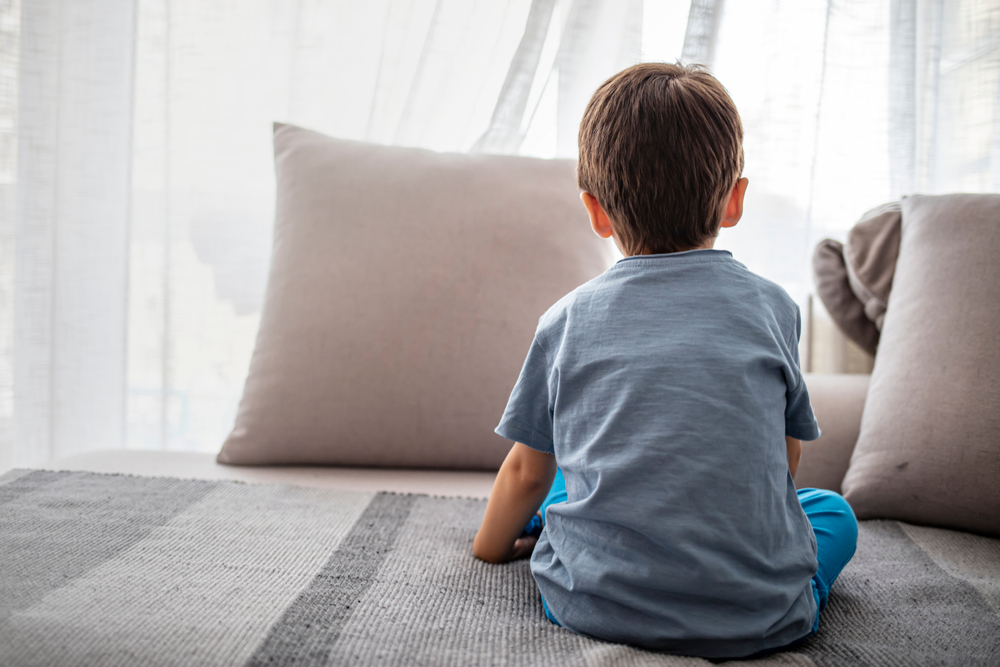 young boy sitting on bed, looking out window